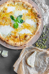 Pizza with four kinds of cheese on the table in the restaurant. Next to spices and different cheese. Vertical image. Natural light. Black background. Top view, flat lay.