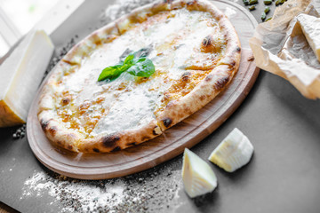 Pizza with four kinds of cheese on the table in the restaurant. Spices, tomatoes  and different cheese near. Horizonal image. Natural light. Black background. 