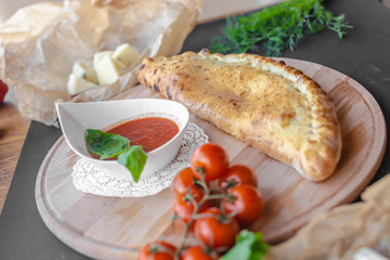 Traditional georgian pie with a bowl of tomato sauce on a wooden plate with tomatoes, cheese and dill near. Horizontal image, black background.