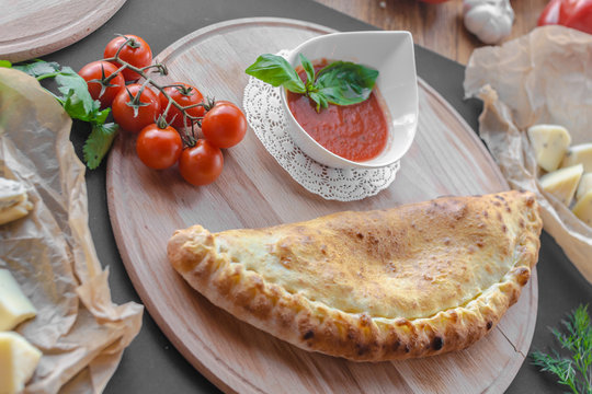 Traditional georgian pie with a bowl of tomato sauce on a wooden plate with tomatoes, cheese and dill near. Horizontal image, black background.