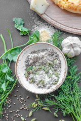 Bowl with spices, parsley, dill and garlic near, part of wooden cooking deck in the corner. Black background, top view, flat lay. Vertical image.