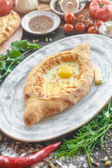 Georgian national pie khachapuri with egg, cheese and butter on the plate, parsley, bowl with caraway, red pepper, vegetables and another pies near. Vertical image. Black background. Top view
