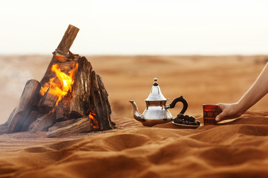 Dates, teapot, cup with tea near the fire in the desert with a beautiful background