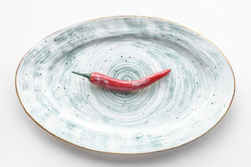 Red hot chili peper lying on white plate with round pattern, white background. Top view, copy...