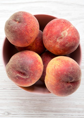 Fresh peaches  in a pink bowl over white wooden background, top view. From above, overhead.