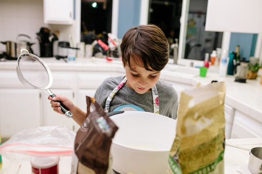 Boy holds a strainer while looking into a mixing bowl