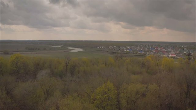 Beautiful village in Russia view from a height.. Green and bright, spring landscape. View of the city and the mountain from the field of flowering trees and young foliage. Juicy fresh grass and vegeta