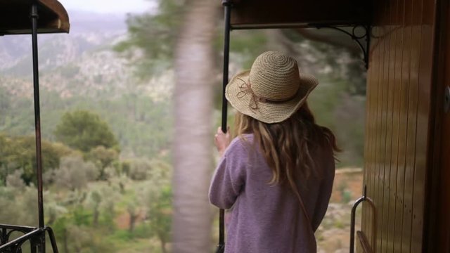 A young woman in a straw hat enjoying traveling on an old train, taking pictures of beautiful tourist locations using vintage camera, feeling excited and happy