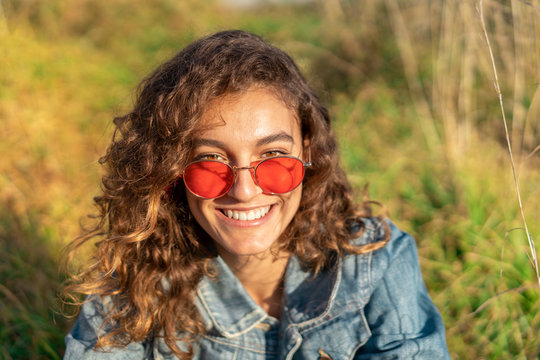 Portrait of happy young woman with curly brown hair wearing red sunglasses