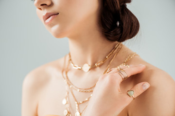 cropped view of young woman with shiny lips in golden necklaces and rings isolated on grey