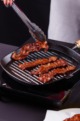 young woman in a gray apron fries bacon