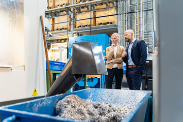 Businessman and businesswoman wearing safety goggles at a machine in factory