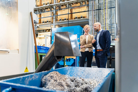 Businessman and businesswoman wearing safety goggles at a machine in factory