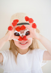 Little cute blond girl with raspberries in her fingers, different emotions, indoor, healthy food summer concept