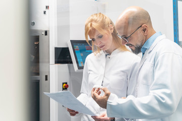 Two technicians wearing lab coats looking at plan