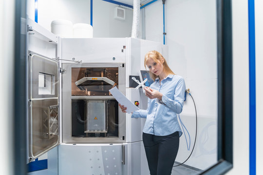 Woman holding paper and workpiece at d printer