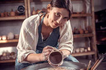 Charming pottery woman works with clay on a potter's wheel. Making pottery.