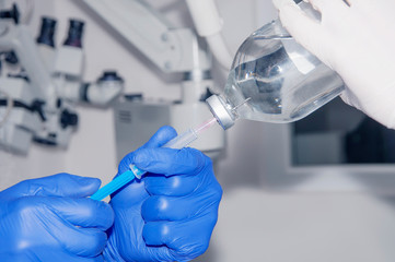 Doctor holds syringe and he gains saline from the bottle