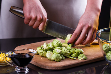 young woman cuts Brussels sprouts on a wooden cutting board