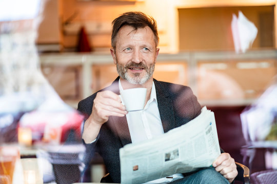 Portrait of smiling mature businessman with newspaper sitting in a coffee shop drinking coffee