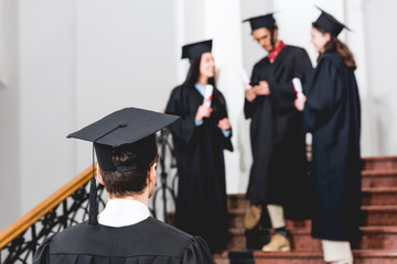 back view of student in graduation cap standing in university