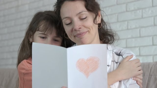 Heart for mom. Mothers Day. Little girl hugs a happy mother reading a postcard from her daughter.