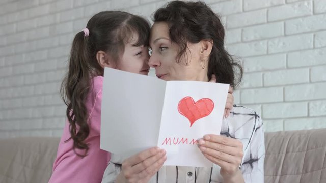 Mothers Day. Little girl hugs a happy mother reading a postcard from her daughter.