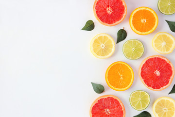 Colorful fruit frame of fresh citrus slices with leaves. Top view, flay lay over a white background with copy space.