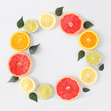 Colorful fruit circle frame of fresh citrus slices with leaves. Top view, flay lay over a white background with copy space.