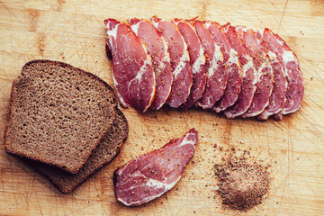 Smoked meat, pepper. Slices of smoked meat with black bread on a wooden board.