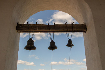 Three church bells in the foreground hanging on a wooden crossbeam in a chapel arch