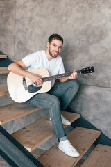 Obraz premium smiling bearded man sitting on stairs and playing acoustic guitar