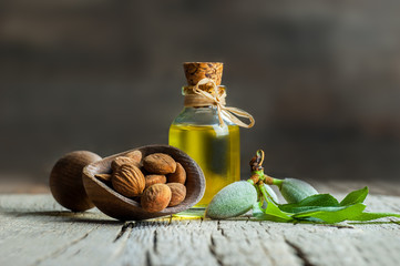 Glass bottle of Almond oil and almond nuts in wooden shovel with green fresh raw almonds on wooden table, almond tree branch