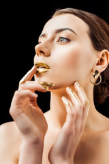 young naked woman with golden makeup and golden paint on fingers touching lips isolated on black