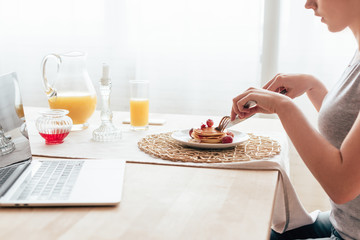 cropped view of young woman eating pancakes in morning
