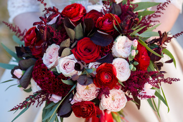 Unsuspected bride holds in her hands an exquisite wedding bouquet of red and pink roses