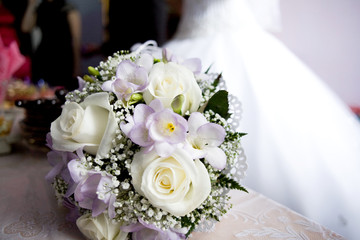 White rose buds in combination with a gray freesia and a sprig of gypsophila in a bouquet of the bride on a blurred background of a wedding dress.
