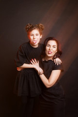 Mother and daughter showing their tongues and grimacing. Black clothes, black background. Mixed light.