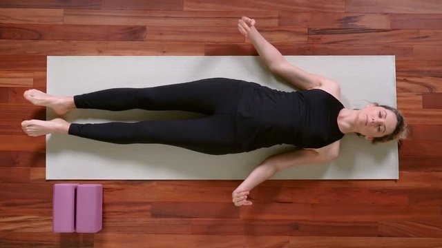 Top view of young woman doing Yoga exercise at home lying down in Shavasana Pose.