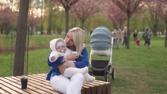 Young mother woman enjoying free time with her baby boy child - Caucasian white child with a parent's hand visible - Dressed in white overall with hearts, mom in blue