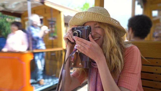 A young woman wearing straw hat enjoying traveling on an old tram or train, taking pictures of beautiful tourist locations using vintage camera, feeling excited and happy