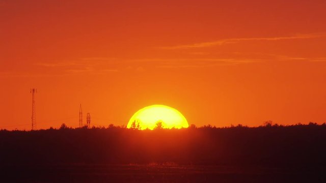 Sunset with a field in the foreground and electric pilones in the distance