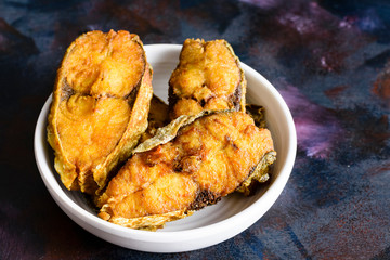 Fries fish slices in a bowl on textured background.