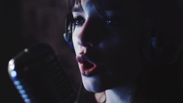 Close up side view of young woman in headphones singing in microphone in the studio. Silhouette of singer. Star, talent, preparing show, studio recording. Profession concept, female portrait
