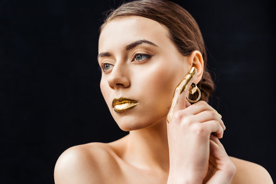 young naked woman with golden makeup and golden paint on finger isolated on black
