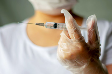 Hands of a physician wearing protective white gloves prepare a syringe shot closeup.