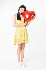 Asian young woman in yellow dress hold  red balloon heart. Young woman holding it with  being excited and surprised  holiday present isolated white  background.concept love surprise valentine day.