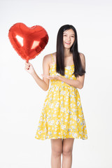 Asian young woman in yellow dress hold  red balloon heart. Young woman holding it with  being excited and surprised  holiday present isolated white  background.concept love surprise valentine day.