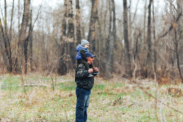 Fototapeta premium Happy weekend concept. happy grandfather and grandson are walking in forest. Spring. Grandpa rolls on the shoulders of a little boy