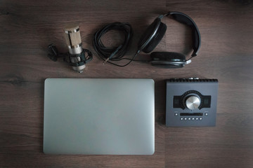 Flat lay of sound designers tools on dark wood table: laptop, sound card, headphones, microphone. Sound engineering tools. Professional sound card for music mixing and mastering